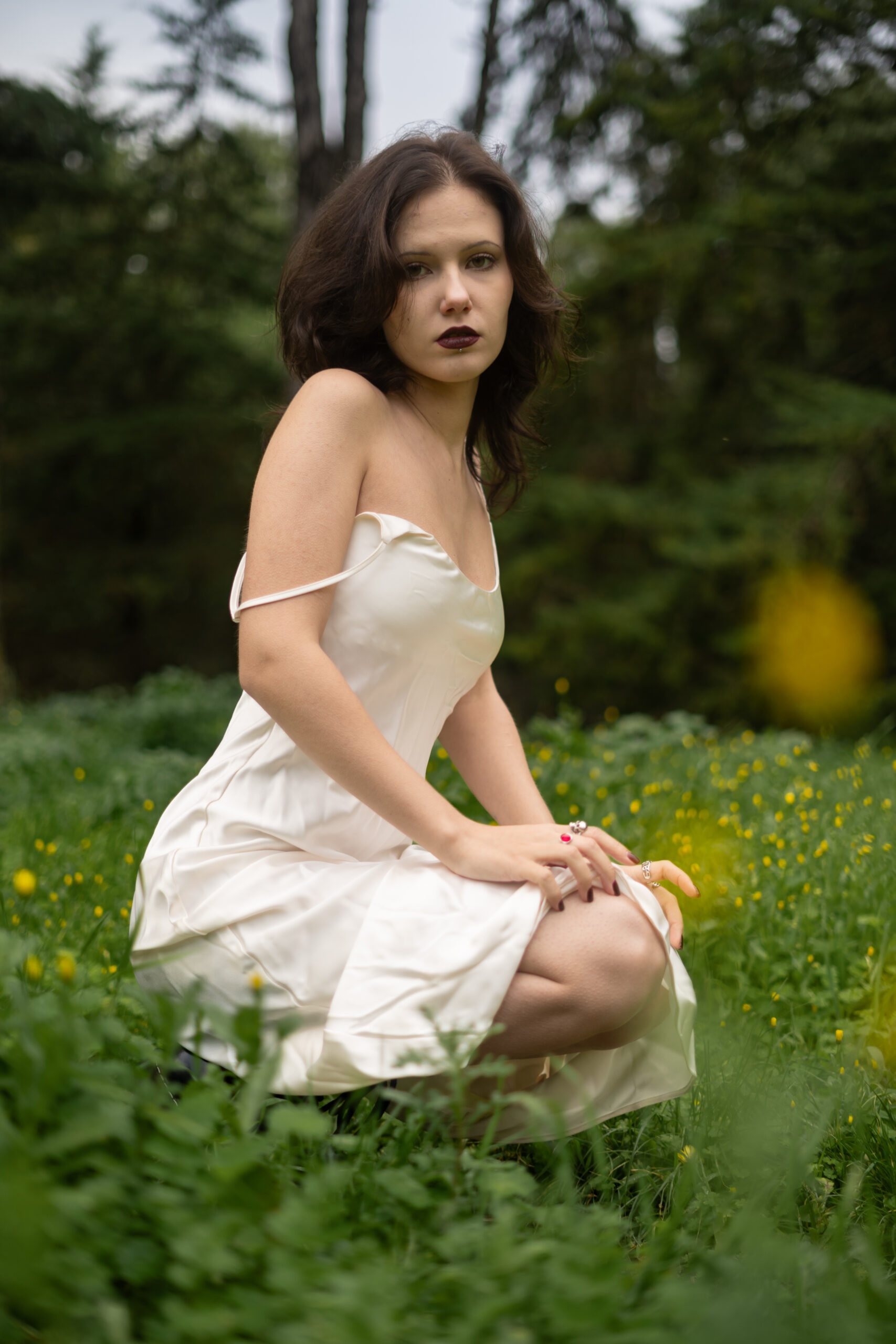 Girl in dark make up sitting in a dark forest surrounded by flowers